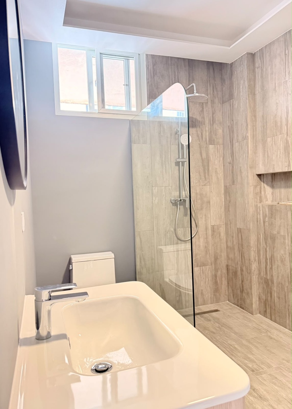 Baño con porcelanato símil madera, lavamanos sobre mueble y ducha en cristal templado